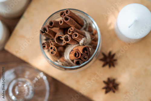 Cinnamon sticks in glass jar, anise star, candles, vintage book on old rustic rustic wooden background. Cozy still life.