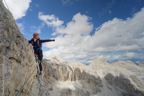 attractive brunette female climber on a steep and exposed Via Ferrata in the Dolomites pointing to the distance