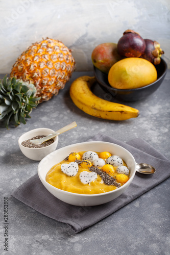 Fototapeta Naklejka Na Ścianę i Meble -  Smoothie bowl on gray background. Delicious mango smoothie topped with chia seeds, pieces of mango and dragon fruit. Healthy breakfast.