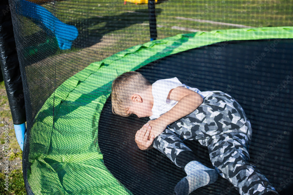 Little boy holding his knee in pain while jumping on trampoline. Stock