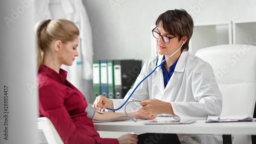 Positive female doctor checking pulse of woman patient using stethoscope medical equipment photo