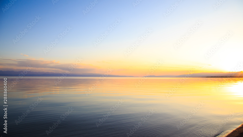 Beautiful sunset on a lake in the mountains. Kyrgyzstan, Issyk-Kul Lake. Bright sky, background in warm colors. Beautiful sunset on a lake in the mountains. Kyrgyzstan, Issyk-Kul Lake. Bright sky, background in warm colors.