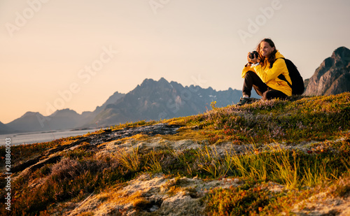 Happy girl traveler with a camera in his hands in Norway, on the Lofoten Islands admires the sunset