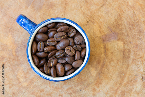 Coffee beans in a hand-painted cup and saucer arranged on a wooden background.