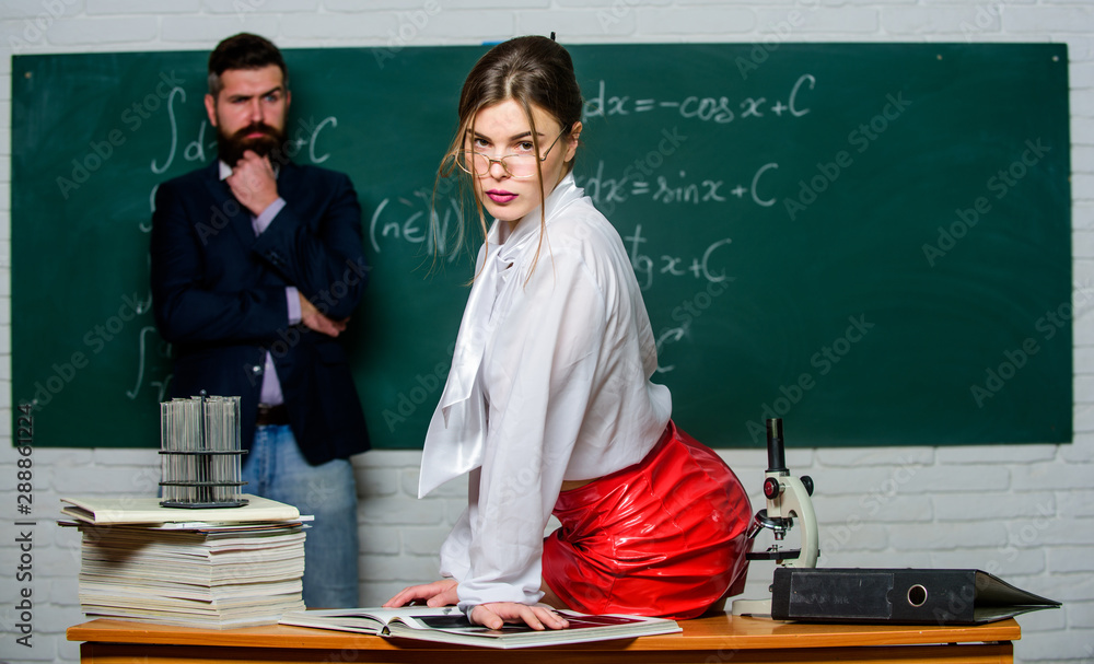 Science is sexy. Everyone dreaming about such teacher. Attractive teacher  in leather skirt. Cheeky teacher. Impudent student. Sexy girl sit table  while man stand chalkboard. Flirting with colleague foto de Stock