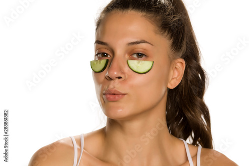 Young woman posing with slices of cucumbers undeer her eyes on white background photo