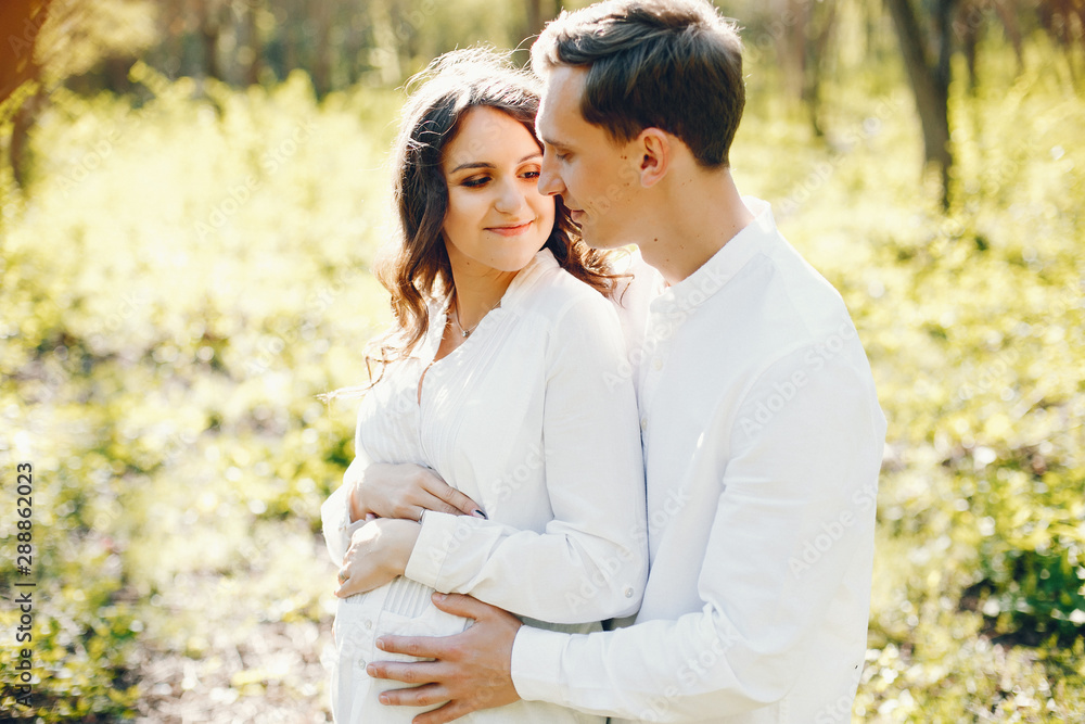 bright and happy pregnant woman walking in the park with her husband