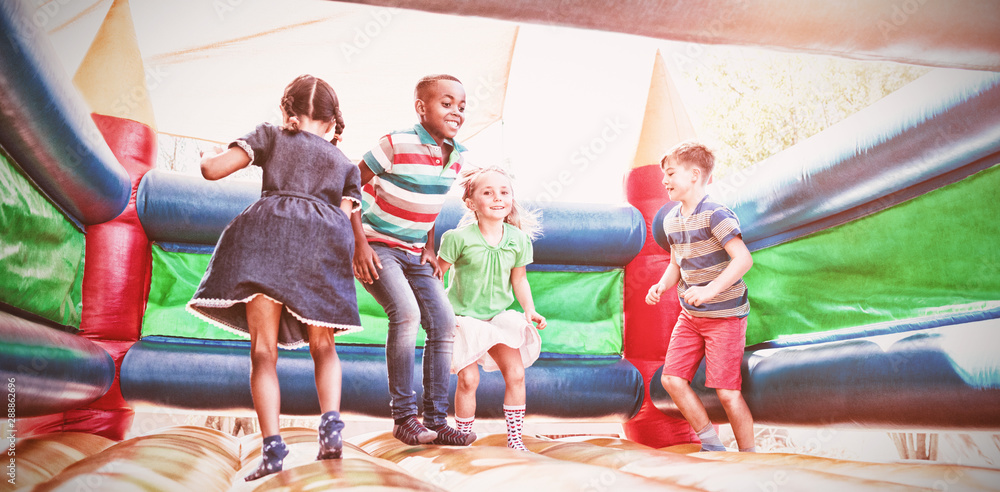 Friends playing on bouncy castle at playground - obrazy, fototapety, plakaty 