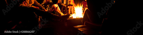 Fototapeta The group of friends are sitting near the bonfire in the night and talking about