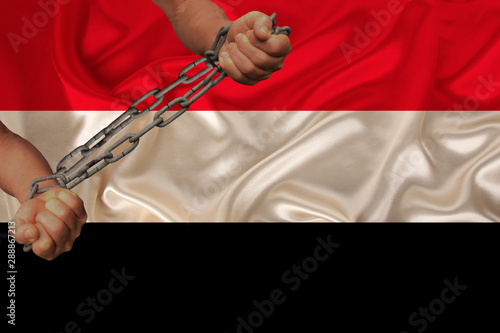 male hands chained in iron chains against the background of the silk national flag of yemen, concept of protest, crime ban, close-up, copy space