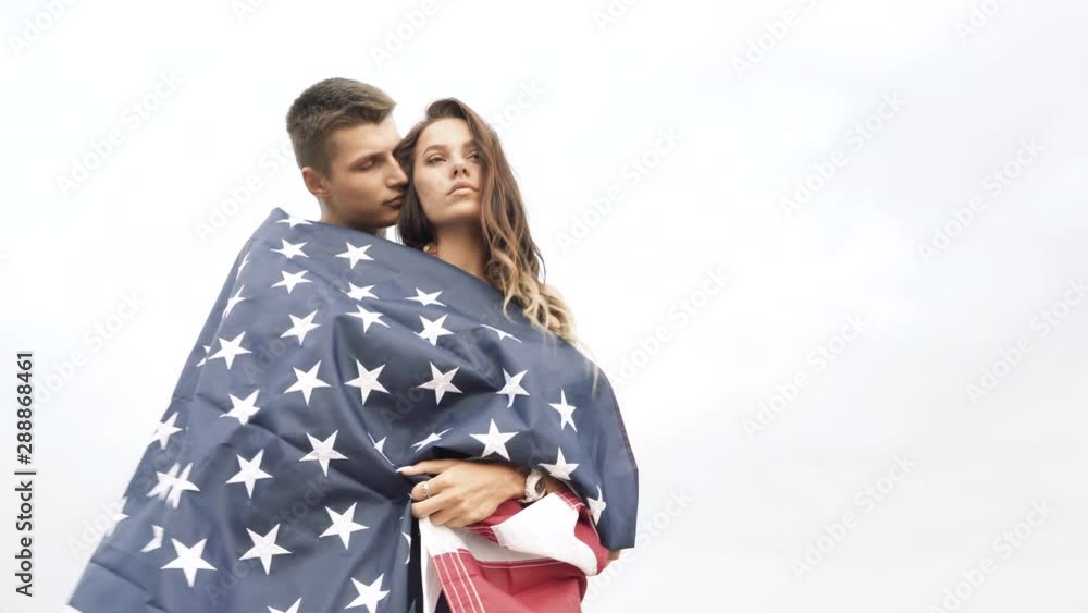 Happy couple hugging and kissing wrapped in an American flag in nature. Independence Day, lifestyle, travel concept. Happy couple hugging and kissing wrapped in an American flag in nature. Independence Day, lifestyle, travel concept.
