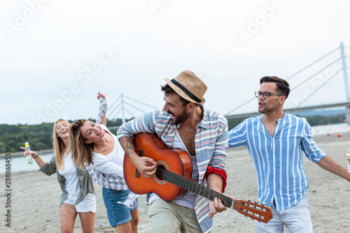 Group of friends hangout at the city beach.One guy plays guitar and singing while his friends dancing around him. © BalanceFormCreative