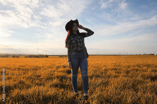 A young girl is traveling around the city hitchhiking. A beautiful young girl went on vacation. A female student in a cowboy hat on the road in autumn. © alexkich