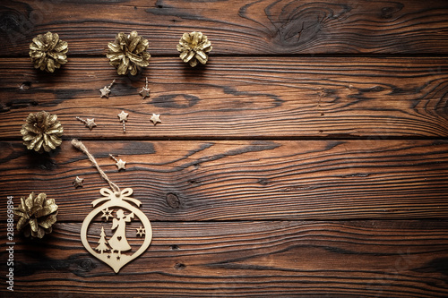 Gilded pine cones, metal stars and wood carved angel Christmas ornament on the dark brown plank wooden surface.