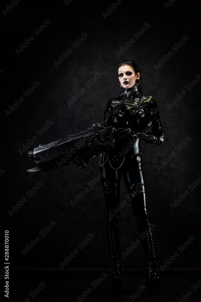 Portrait of a young woman in latex jumpsuit holding a big futuristic weapon in her hands Portrait of a young woman in latex jumpsuit holding a big futuristic weapon in her hands