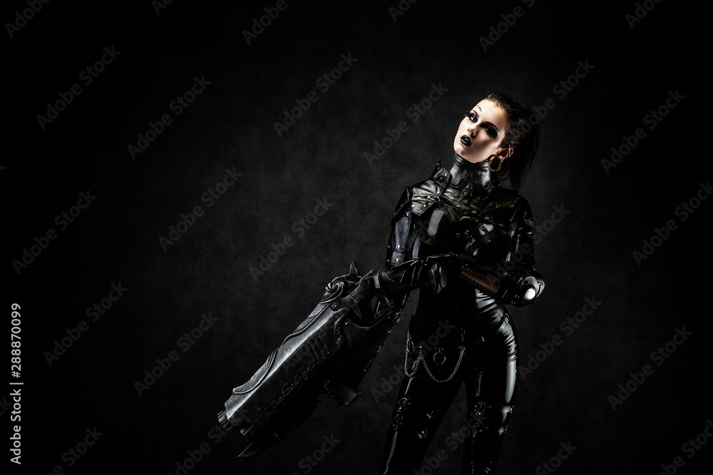Portrait of a young woman in latex jumpsuit holding a big futuristic weapon in her hands Portrait of a young woman in latex jumpsuit holding a big futuristic weapon in her hands