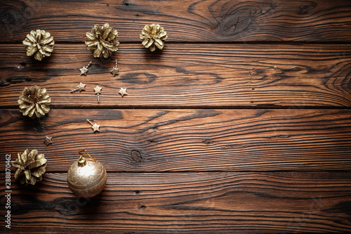 Gilded pine cones, metal stars and sparkling Christmas ball on the dark brown plank wooden surface.