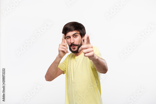 Happy brunet bearded man in a yellow t-shirt with moustaches pointing with fingers at the viewer. Concept of positive emotion thinking. Lucky you!