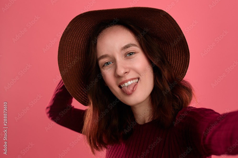 Excited beautiful brunette girl in a wide-brimmed hat making selfie standing on a dark pink background. Excited beautiful brunette girl in a wide-brimmed hat making selfie standing on a dark pink background.