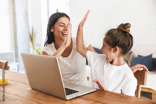 Quadro su tela Image of excited family woman and her little daughter giving high five and using