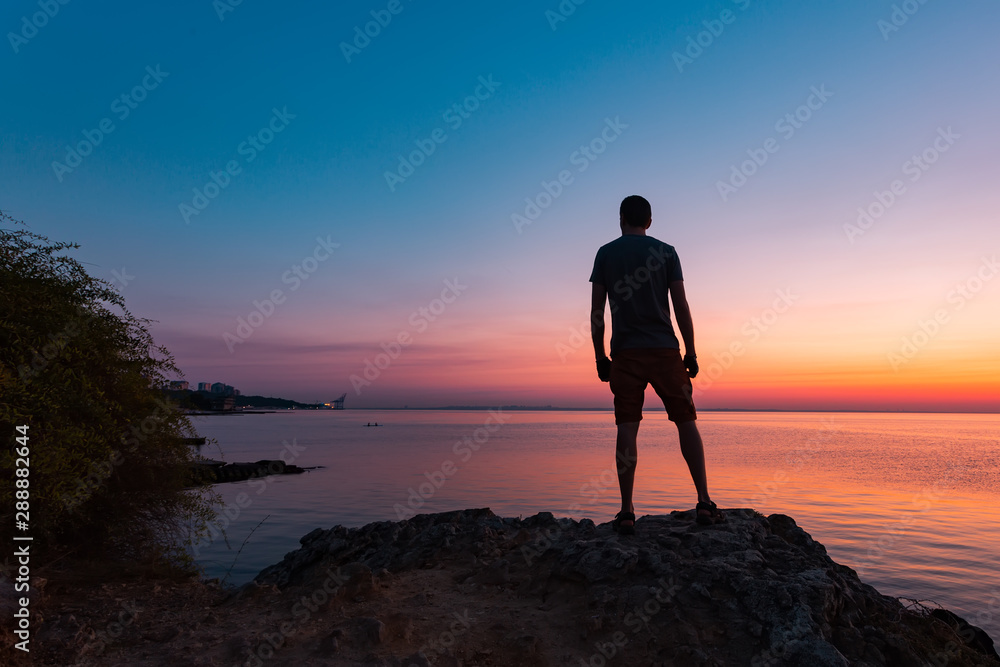 Silhouette of lonely man standing on the rocks and exploring the sea bay