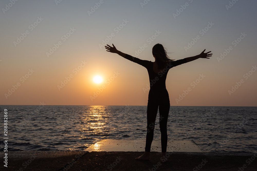 A silhouette of slim body woman on the sea enjoing the sunrise