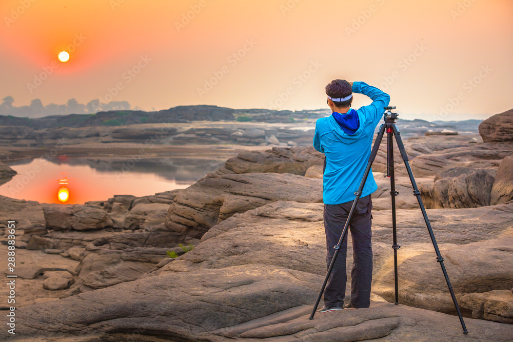 Man photographer take a photo at Sam Phan Bok camera and tripod, Sunrise new day, the biggest rock reef in the Mae Khong River as the Grand Canyon of Thailand in Ubon Ratchathani and beautiful sky