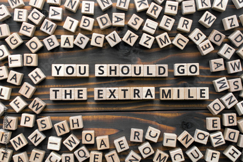 You should go the extra mile - phrase from wooden blocks with letters, to make a special effort try harder concept, random letters around, white  background