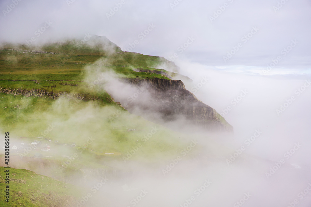 Outstanding foggy landscape of Mykines island with small village and green mountains. Faroe Islands. 