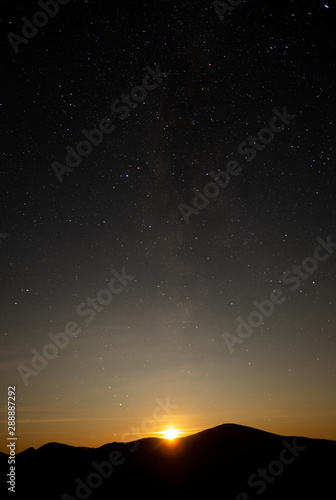 The moon setting behind mountains below a clear stary nights sky