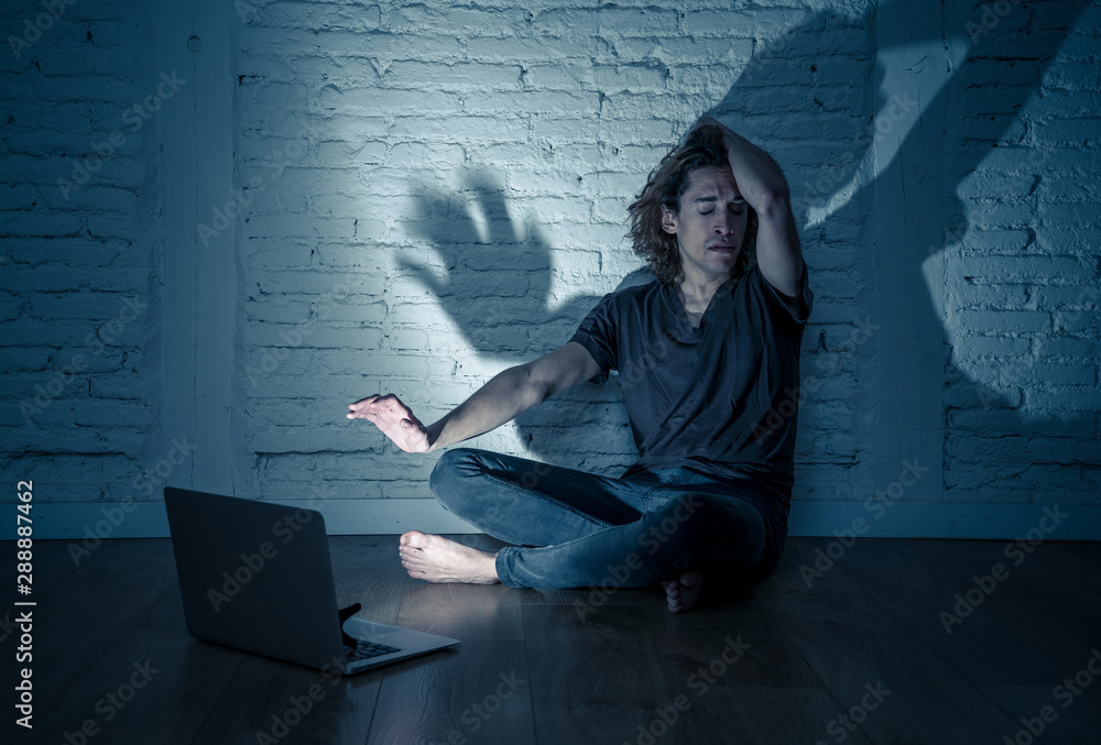 Teenager man suffering Internet cyber bullying sitting alone with computer feeling hopeless Teenager man suffering Internet cyber bullying sitting alone with computer feeling hopeless