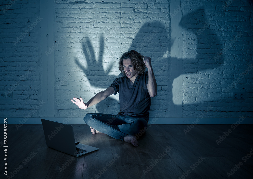 Teenager man suffering Internet cyber bullying sitting alone with computer feeling hopeless Teenager man suffering Internet cyber bullying sitting alone with computer feeling hopeless