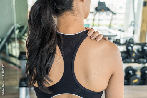 Asian woman holding her shoulder at the gym. Shoulder or back injury during training