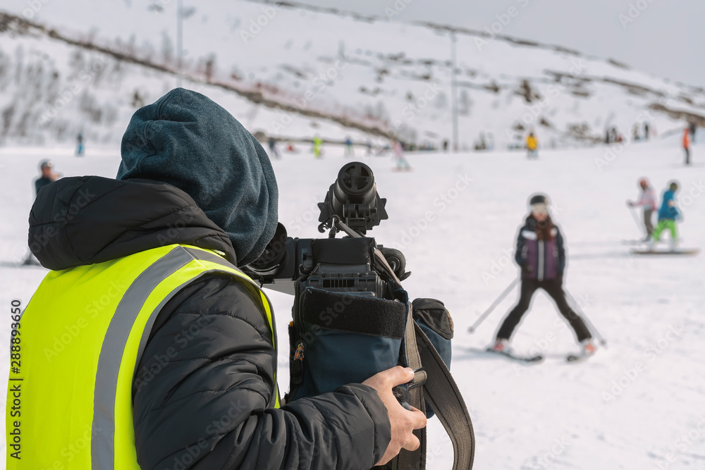 Behind the scenes. Unrecognizable operator with video camera, rear view, shooting sports scenes outdoors, on a ski slope Behind the scenes. Unrecognizable operator with video camera, rear view, shooting sports scenes outdoors, on a ski slope