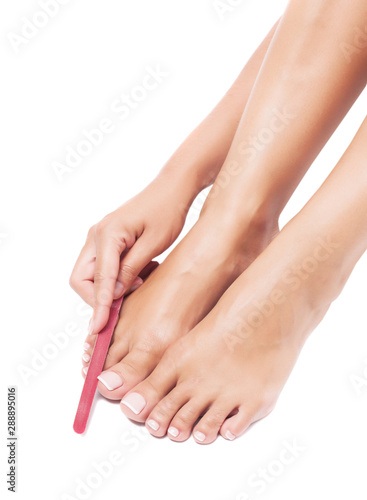 Woman is doing herself pedicure on a white background in the studio. © murika