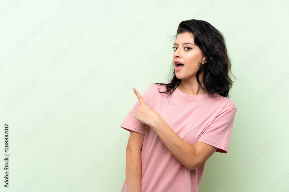 Young woman over isolated green background surprised and pointing side Young woman over isolated green background surprised and pointing side