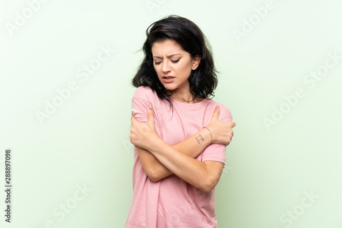 Young woman over isolated green background freezing