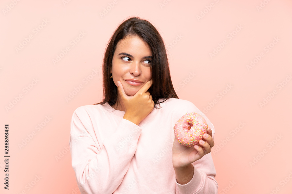 Young girl holding a donut over isolated pink background thinking an idea Young girl holding a donut over isolated pink background thinking an idea
