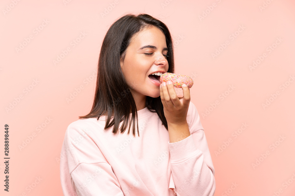 Young girl holding a donut over isolated pink background Young girl holding a donut over isolated pink background
