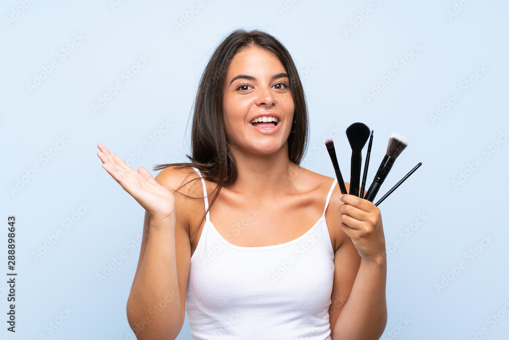 Young girl holding a lot of makeup brush with shocked facial expression Young girl holding a lot of makeup brush with shocked facial expression