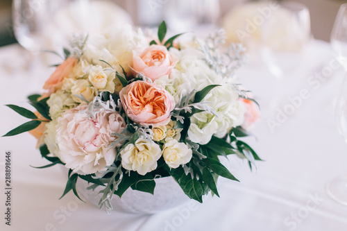 Fine wedding floral arrangement with pink peonies  white roses  dusty miller  and greenery  silver vase  white tablecloth  luxury wedding reception decor