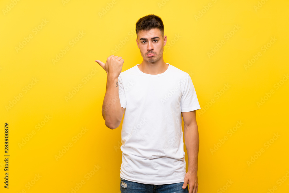 Young handsome man over isolated yellow background unhappy and pointing to the side Young handsome man over isolated yellow background unhappy and pointing to the side