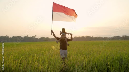 father carrying little girl pride flapping Indonesian flag with happiness in the rice field photo