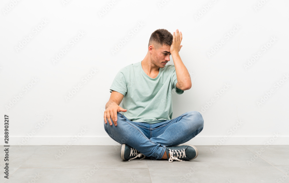 Young handsome man sitting on the floor having doubts with confuse face expression Young handsome man sitting on the floor having doubts with confuse face expression