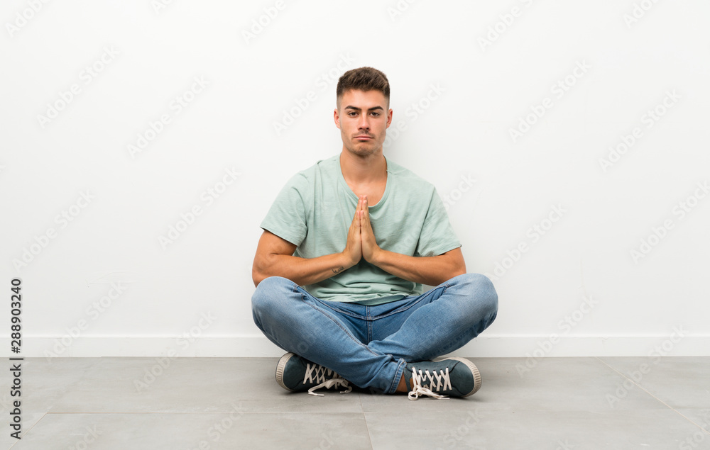 Young handsome man sitting on the floor pleading Young handsome man sitting on the floor pleading