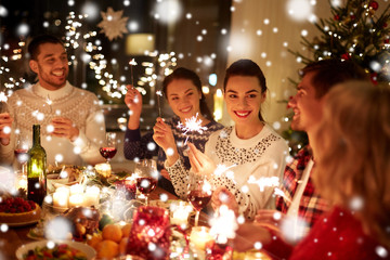winter holidays and people concept - happy friends with sparklers celebrating christmas at home feast over snow