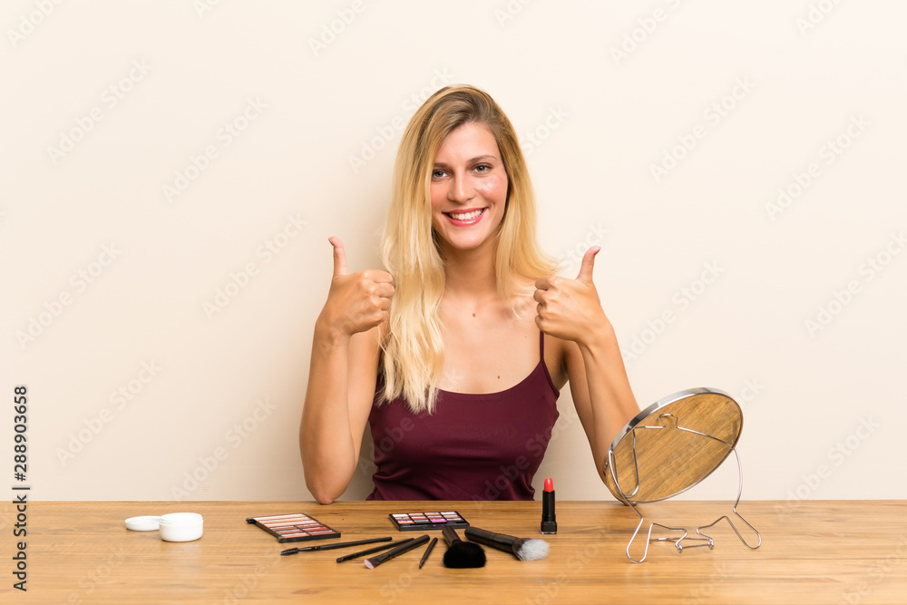 Young blonde woman with cosmetic in a table giving a thumbs up gesture