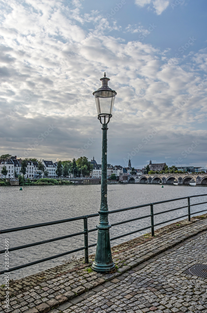 Traditional lantern on Stenenwal (Stone Wall) quay on the east bank of the river Maas in Maastricht, The Netherlands, with the town center on the other bank in the background
