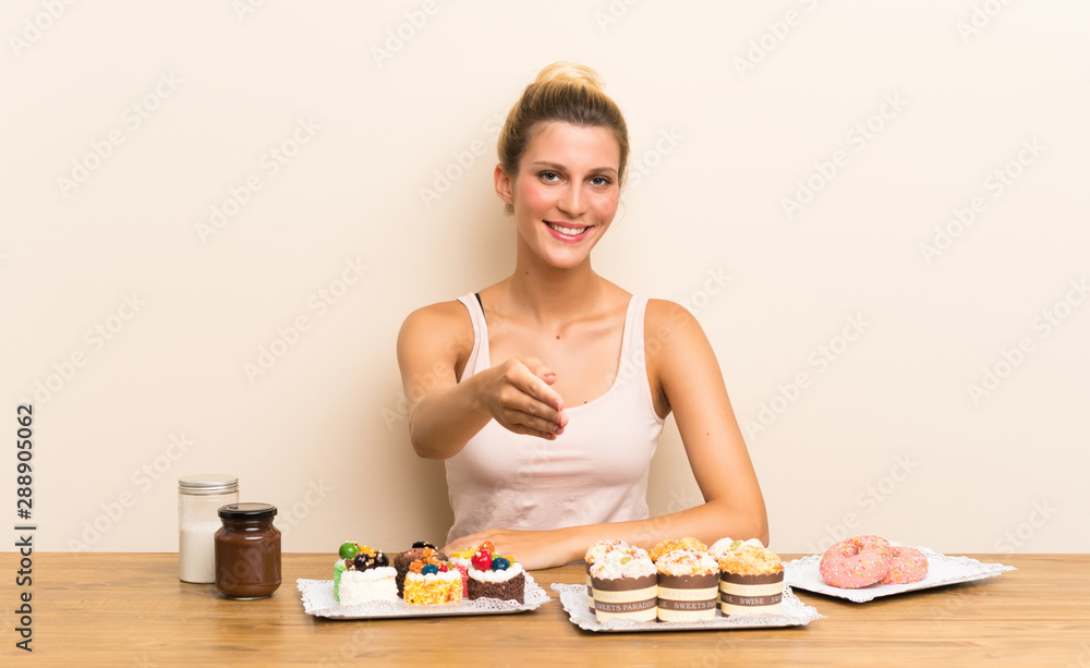 Young woman with lots of different mini cakes in a table handshaking after good deal Young woman with lots of different mini cakes in a table handshaking after good deal