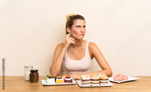 Young woman with lots of different mini cakes in a table thinking an idea
